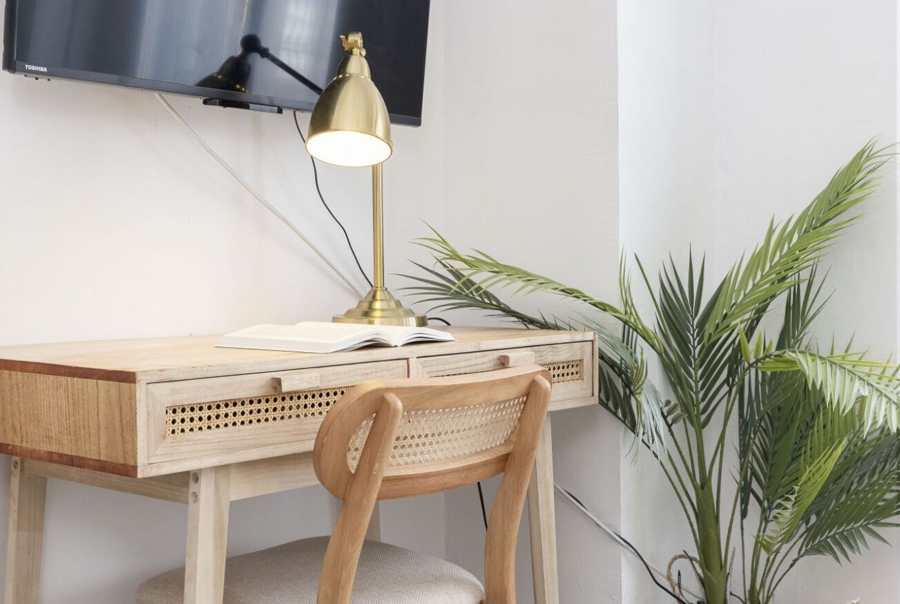 Een houten bureau met een lamp, een stoel en een plant.