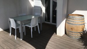 En uteplats med ett glasbord och vita stolar, en trätrumma och en skjutdörr i glas.