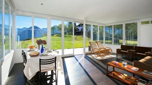 Une pièce spacieuse dotée d’une grande table à manger, de sièges confortables et offrant une vue sur un paysage montagneux grâce à de grandes fenêtres.