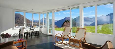 A spacious room with large windows, a dining area, and a seating area with wicker chairs.