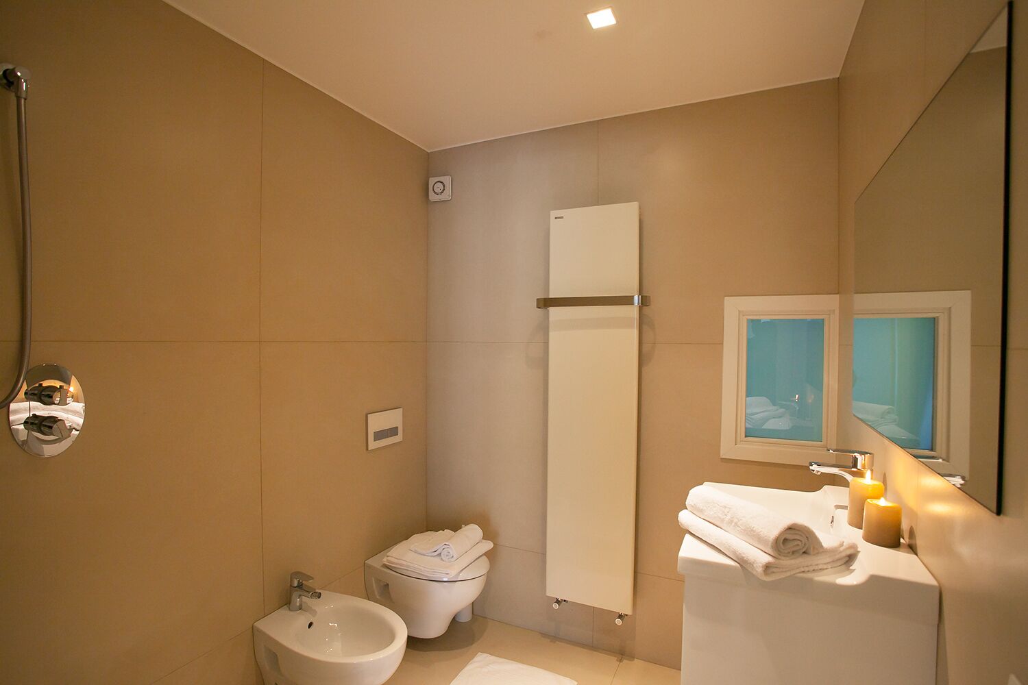Un baño moderno con bidé, inodoro, lavamanos y un espejo con vista a la ventana.