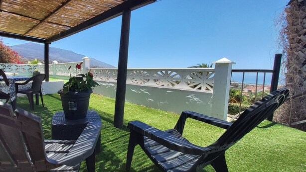 A covered outdoor seating area with a table and chairs, a potted plant, and a view of a mountain and ocean. - Little house with pool on La Palma (Los Llanos de Aridane)
