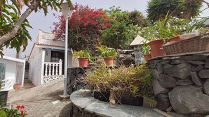 A garden with potted plants, a stone wall, and a white building with a balcony. - Little house with pool on La Palma (Los Llanos de Aridane)