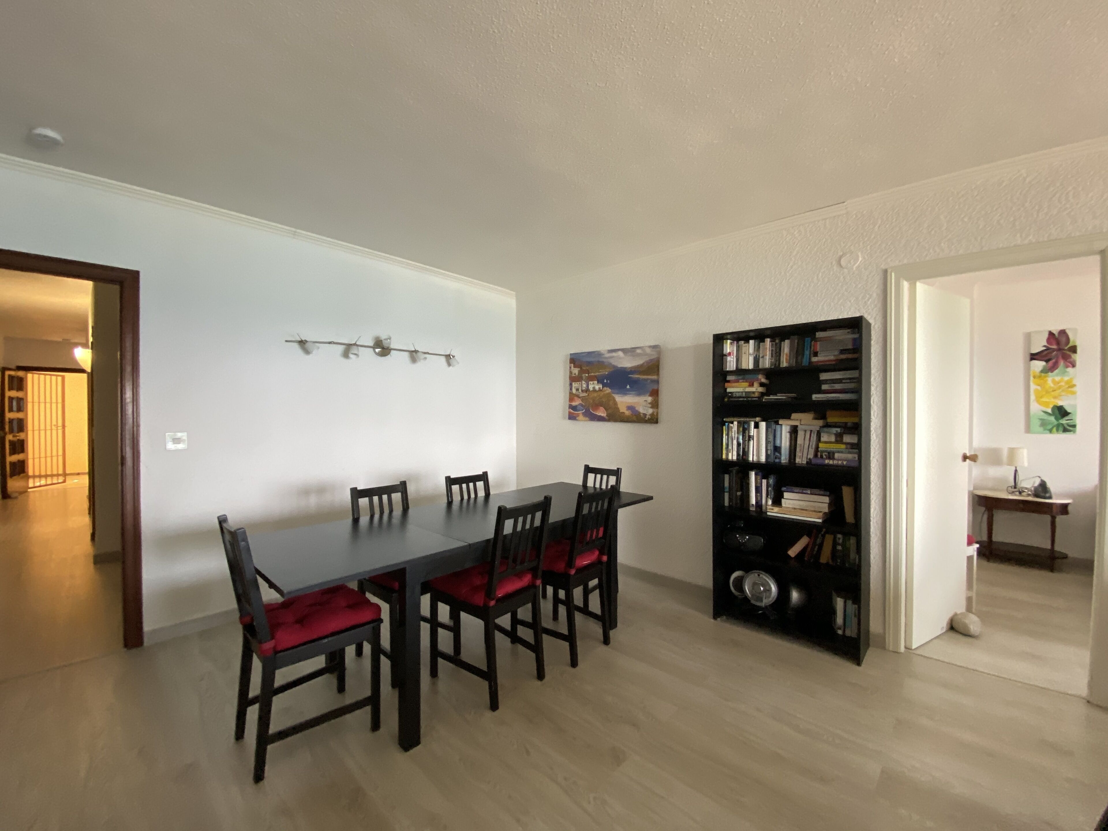 Een eetruimte met een lange tafel, zes stoelen, een boekenkast en een schilderij aan de muur.