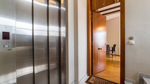 L’entrée d’un hôtel, avec un ascenseur moderne et une porte en bois donnant sur un espace dédié à la restauration.