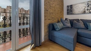 Un salon avec un canapé bleu, un mur en briques apparentes et une grande fenêtre donnant sur des immeubles.