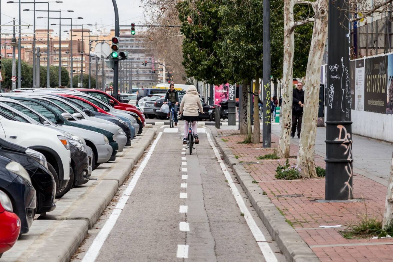 Eine Straße mit parkenden Autos, einem Radfahrer und einem Fußgänger.