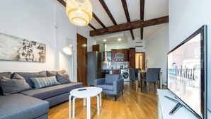 Un salon moderne avec un canapé gris, une petite table blanche et une cuisine en arrière-plan.
