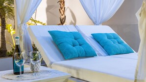Un transat agrémenté de deux coussins bleu vif, une bouteille de vin et un verre posés sur une table recouverte d’une nappe blanche.