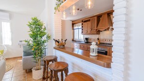 Une cuisine moderne avec des meubles en bois, un mur recouvert de briques blanches et un coin bar avec des tabourets.