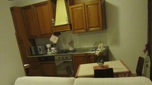 Una sala de estar con un sofá blanco, armarios de madera, una cocina con estufa y microondas, y una mesa de comedor con sillas.