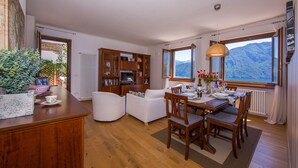 A spacious living area with a wooden dining table, white sofas, and a view of mountains through large windows.
