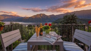 A balcony with a table, chairs, a bottle, glasses, and flowers.