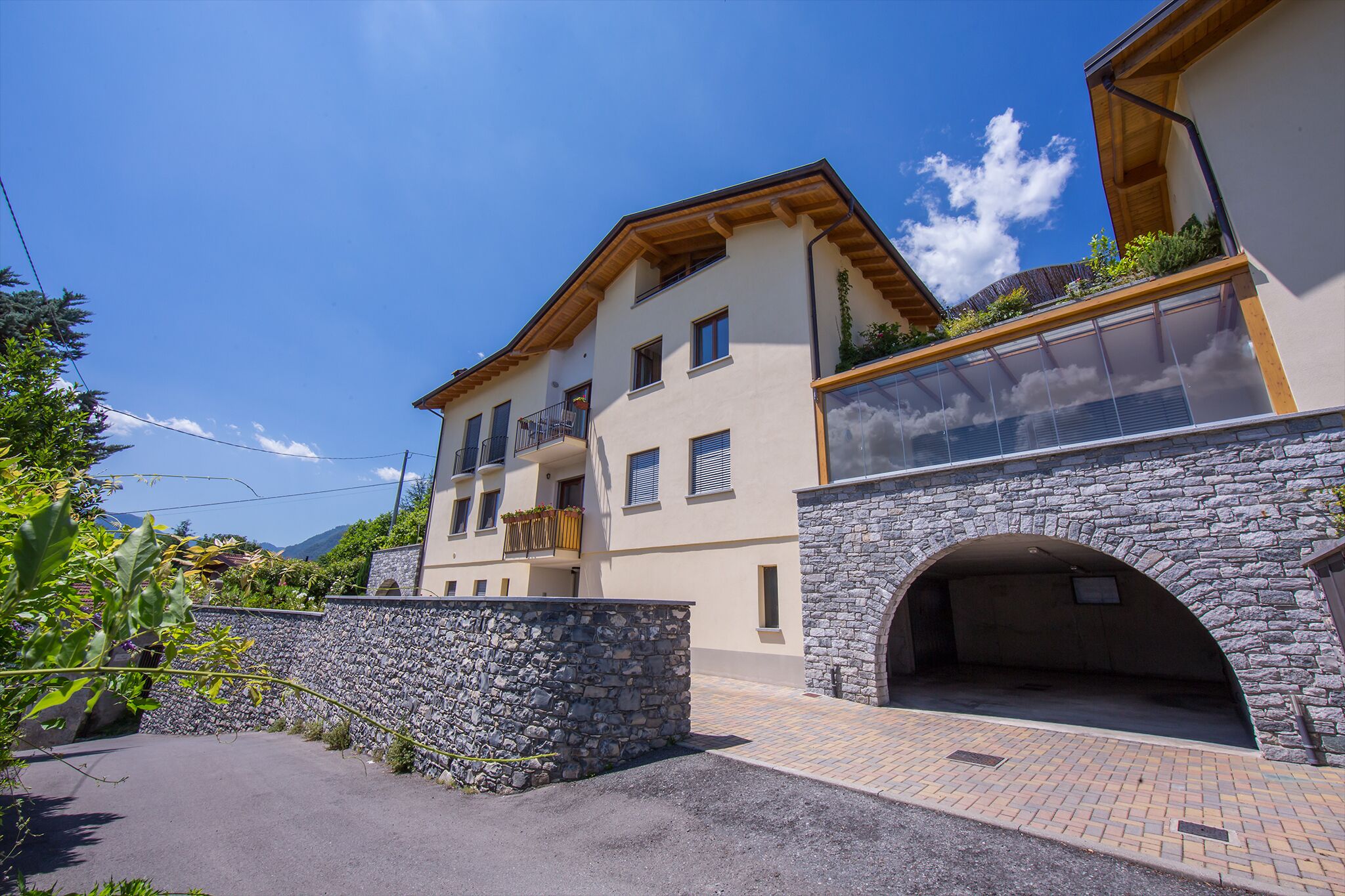 A multi-story building with a stone archway entrance, balconies with plants, and a clear sky.