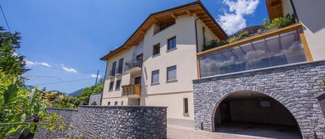 A multi-story building with a stone archway entrance, balconies with plants, and a clear sky.