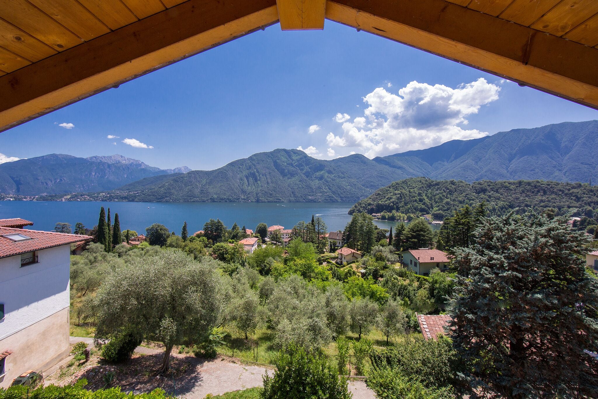 Une vue depuis un balcon en bois donnant sur un lac, des montagnes et un village avec ses maisons et ses arbres.