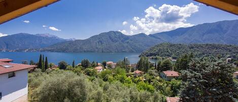 Une vue depuis un balcon en bois donnant sur un lac, des montagnes et un village avec ses maisons et ses arbres.