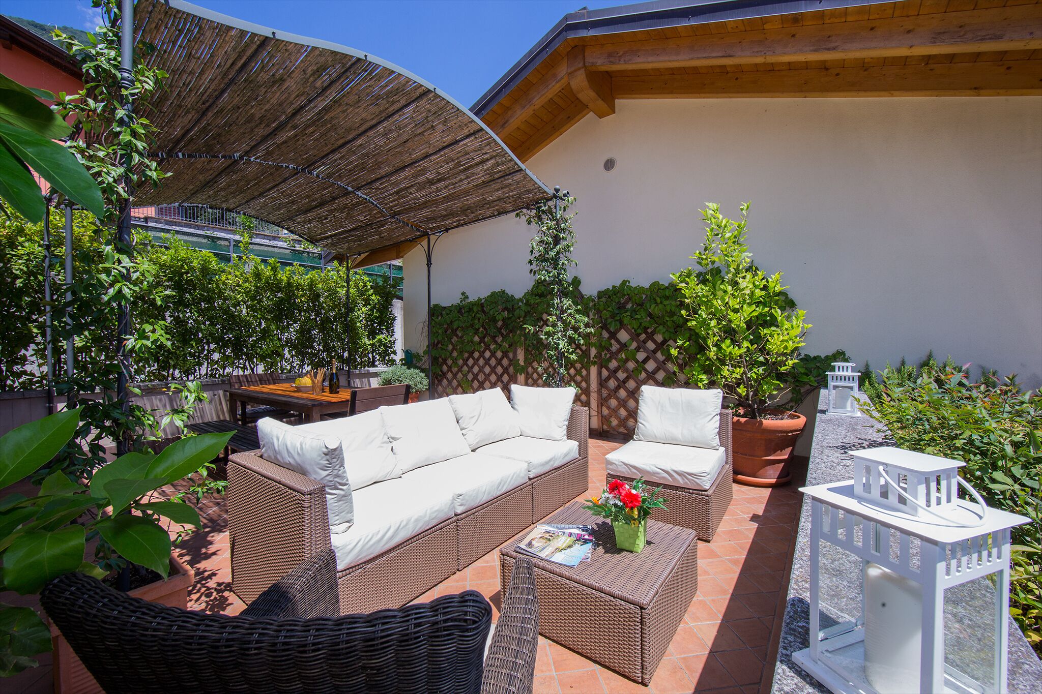 A patio area with wicker furniture, a table with a magazine, and potted plants.