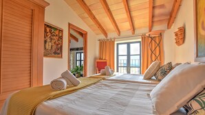 Quarto de hotel com duas camas, vigas de madeira no teto, uma janela grande com cortinas e um quadro na parede.