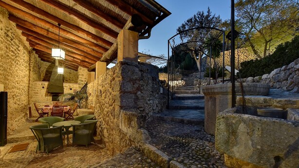 Pátio de pedra com pérgola de madeira rústica, área de estar ao ar livre e escadaria de pedra que leva a um nível superior.