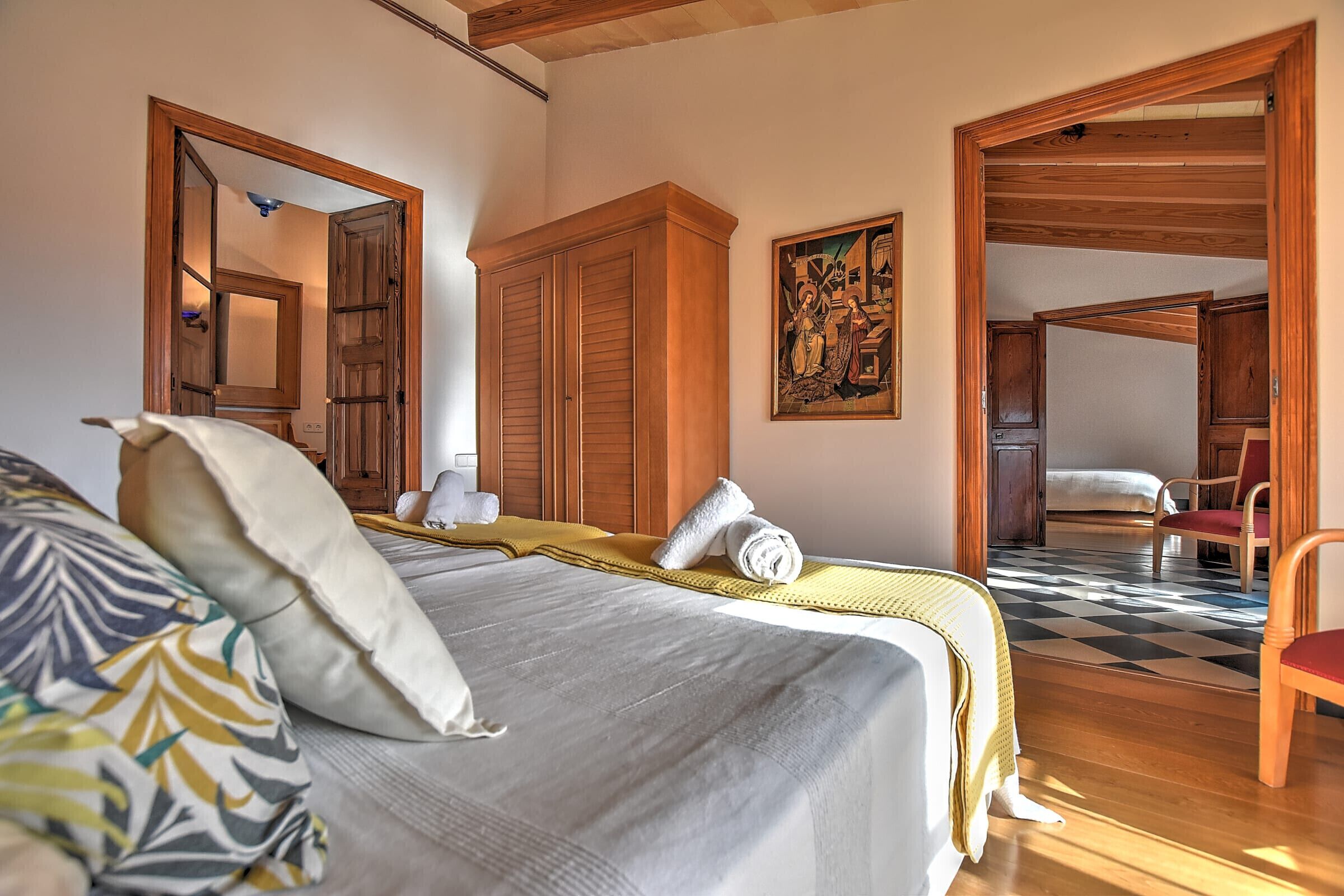Een slaapkamer met een groot bed, een houten garderobe, een schilderij en een geruite vloer.