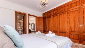 A bedroom with a large bed, wooden wardrobe, and a bathroom visible through an open door. - Villa Sa Cabaneta with pool, tennis court, and views to the Palma Bay (Marratxi)