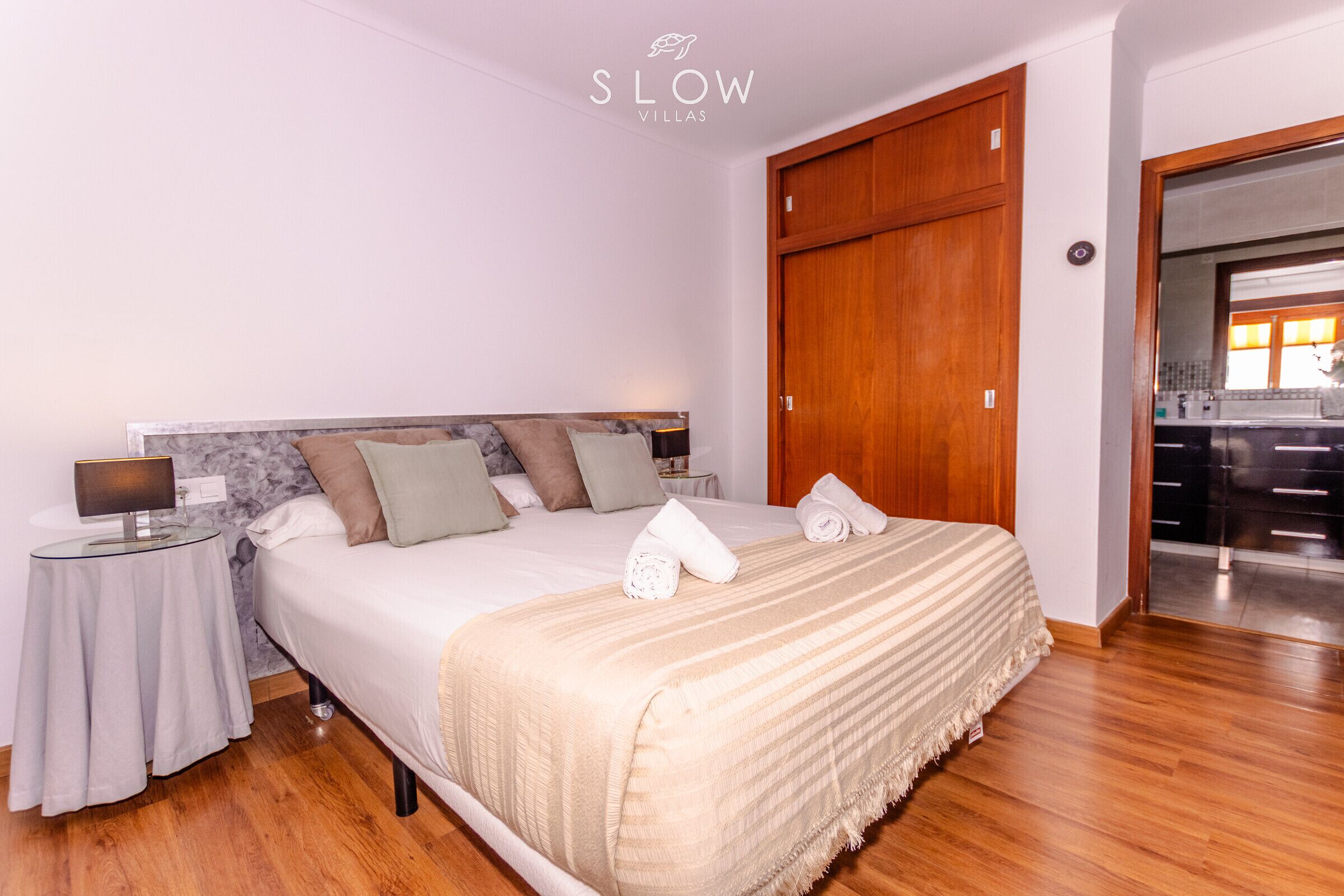 A bedroom with a bed, a nightstand, a wooden wardrobe, and a bathroom visible through an open door.