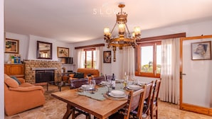 A dining area with a wooden table set for four, surrounded by chairs. There is a fireplace with a stone mantle, a sofa, and a television in the background. - Villa Sa Cabaneta with pool, tennis court, and views to the Palma Bay (Marratxi)