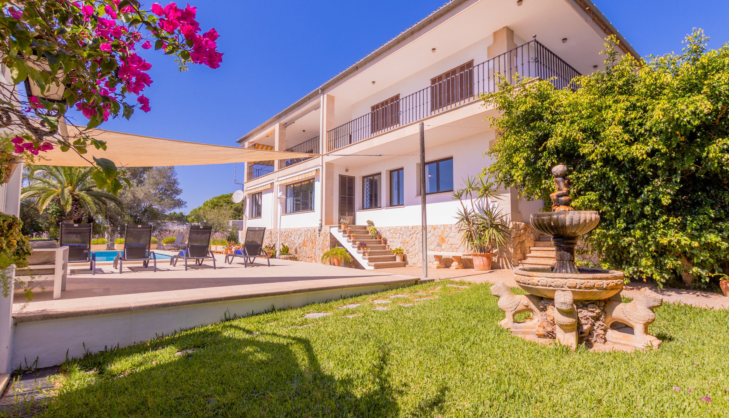 Una villa de dos pisos con piscina, mobiliario exterior y una fuente.