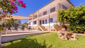 Una villa de dos pisos con piscina, mobiliario exterior y una fuente.