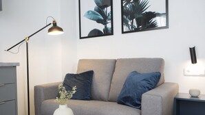 A modern living room with a grey sofa, two blue cushions, a white vase with flowers, a black floor lamp, and framed botanical prints on the wall. - Singular Stays Parque Central VIII (Valencia)