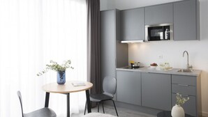 A modern kitchen with grey cabinets, a built-in microwave, and a sink. There is a round table with a vase of flowers and a chair. - Singular Stays Parque Central VIII (Valencia)