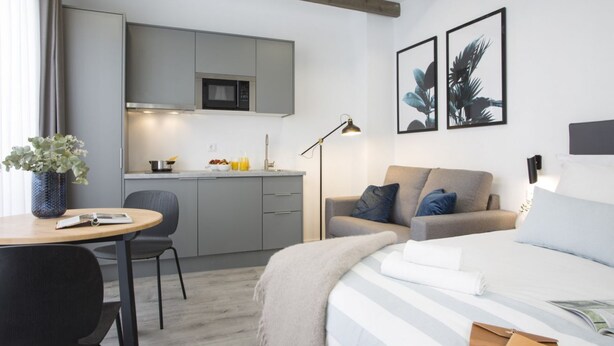 A modern hotel room with a bed, a desk, a chair, a sofa, and a kitchenette. - Singular Stays Parque Central VIII (Valencia)