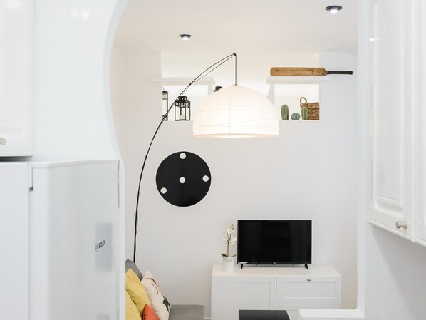 A modern living room with a flat-screen TV, a white cabinet, a lamp, and a ceiling light fixture.