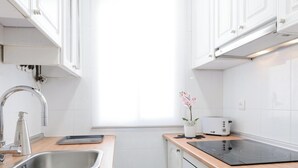 A modern kitchen with white cabinets, a stainless steel sink, a toaster, and a black induction cooktop. - Atocha - 2-Bedroom Apartment in Downtown Madrid (Madrid)