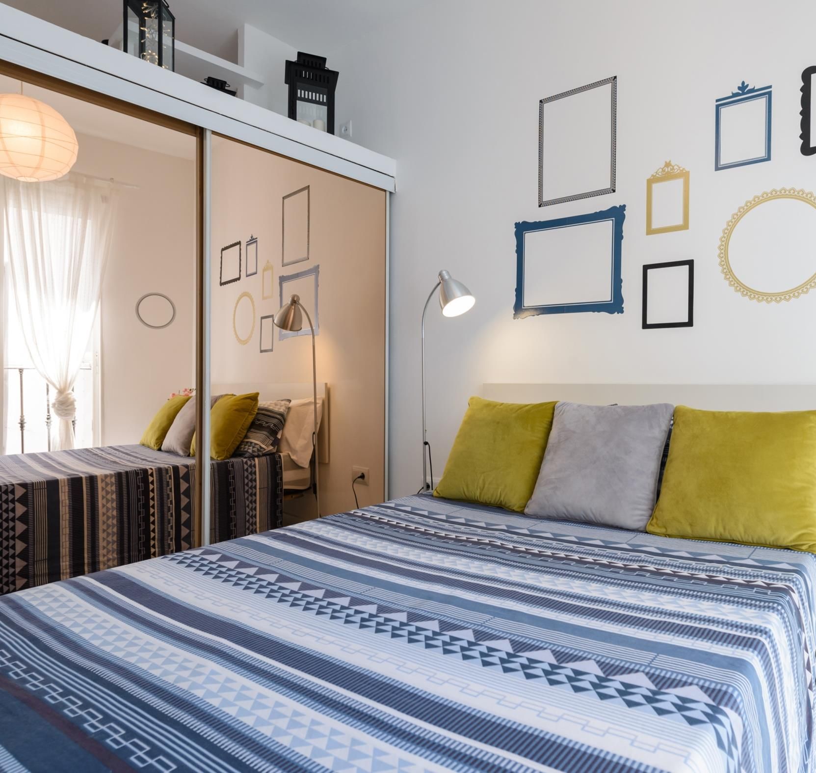 Un dormitorio con cama, almohadas, mesita de noche, lámpara y adornos en la pared.