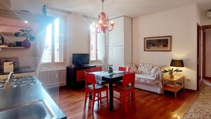 A spacious living area with a dining table, red chairs, a sofa, a TV, and a kitchen with a sink and stove.