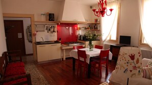 A compact kitchen with a red backsplash, a dining area with red chairs, and a white sofa with floral patterns.