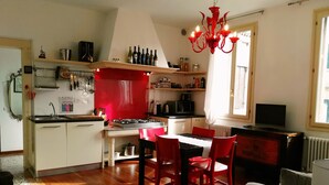 A compact kitchen with a dining area, a red chandelier, and a window providing natural light.