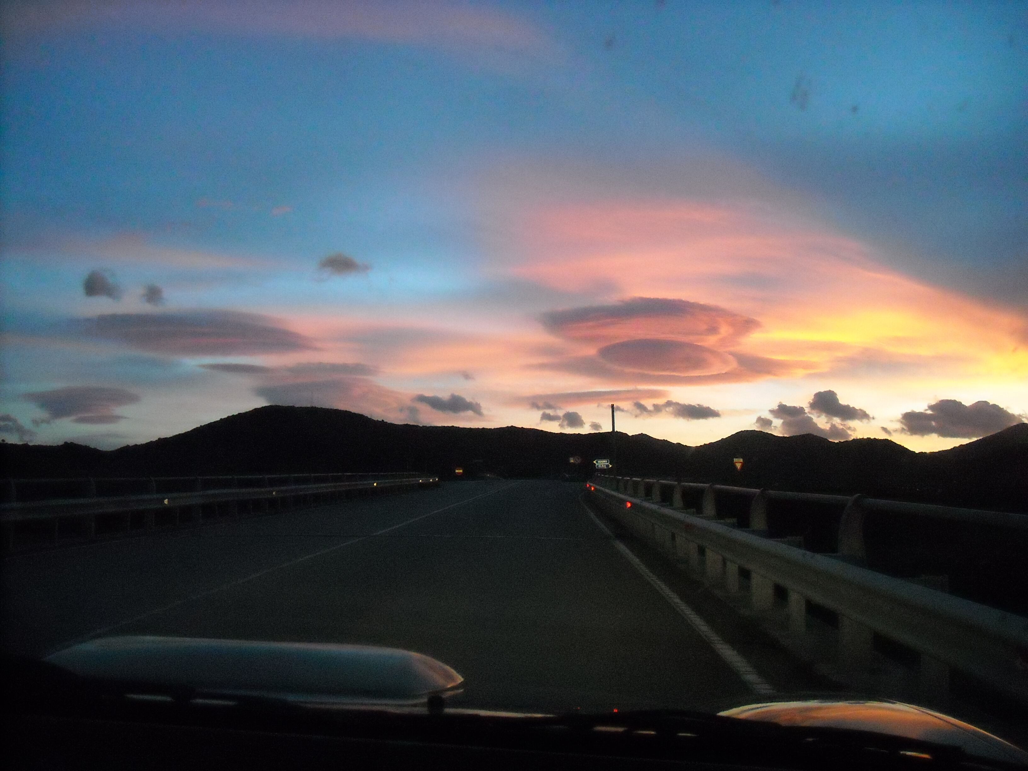Uma estrada com barreira de proteção e céu ao pôr do sol.