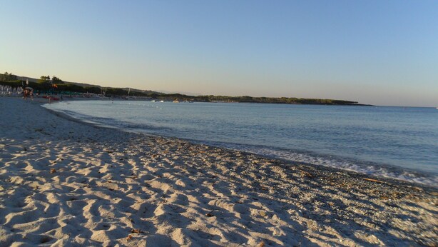 En strand med klar himmel, sandstrand och stilla vatten.