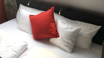 A bed with white bedding and a red pillow, two bedside lamps, and a dark headboard.
