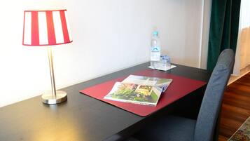 A hotel room with a desk, a television, a lamp, a water bottle, and a magazine.