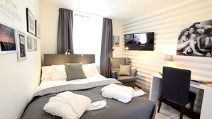 Quarto de hotel com cama, escrivaninha, cadeira, televisão e parede com quadros.