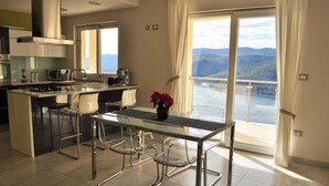A modern kitchen with a central island, clear chairs, and a view of a mountainous landscape through large windows. - New apartment (128m2), terrace, sea view, A / C, Free Wifi & parking  (Rabac)