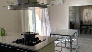 A modern kitchen with a gas stove, a pot on the stove, and a green toaster. There is a dining area with a glass table and chairs. - New apartment (128m2), terrace, sea view, A / C, Free Wifi & parking  (Rabac)