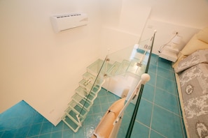 A modern bathroom with a glass shower enclosure, a white air conditioning unit, and a patterned bath mat.