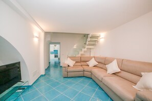 A modern living room with a beige sectional sofa, a flat-screen TV, and a staircase with white railings.