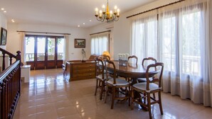 A spacious dining area with a round table and chairs, a chandelier, and large windows with curtains. - Can Soler - Beautiful chalet with private pool in Alcanada (Alcúdia (Alcanada))