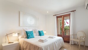 A neatly arranged bedroom with a bed, pillows, a nightstand, a chair, and a view of the outdoors. - Can Soler - Beautiful chalet with private pool in Alcanada (Alcúdia (Alcanada))